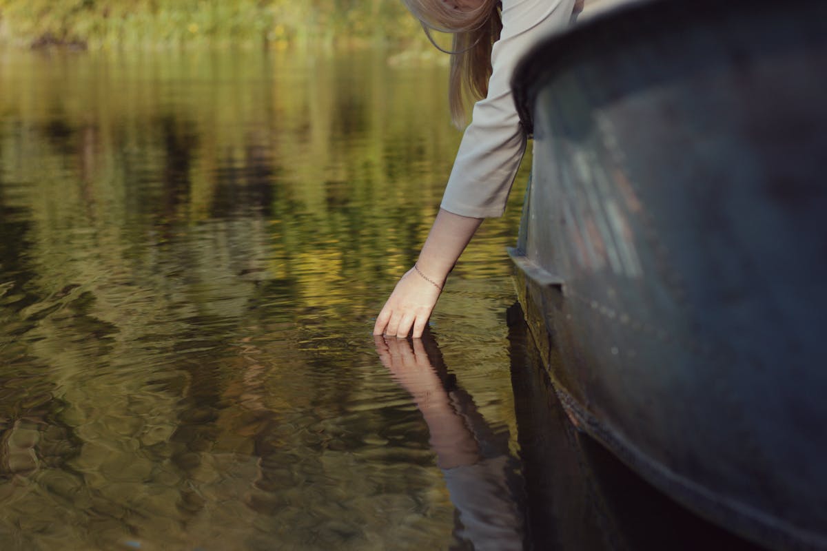 Detail of a hand trailing in lake water from the side of a wooden boat