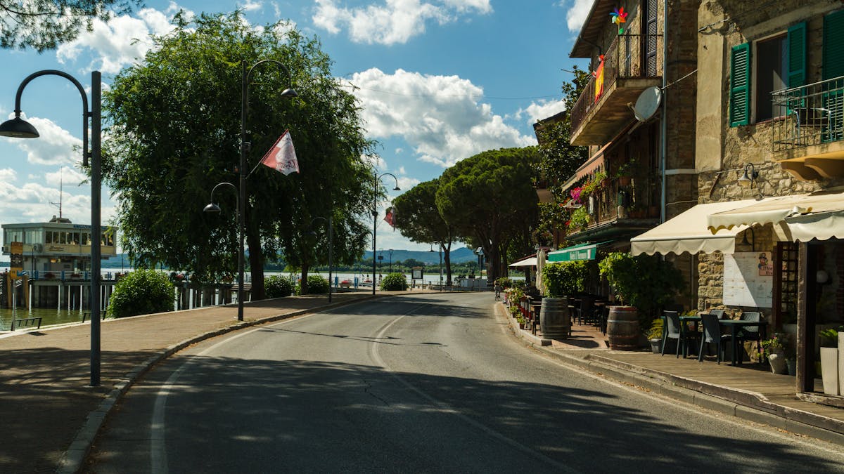 The lakeside promenade in Bardolino with plane trees, outdoor cafe tables, and Lake Garda visible beyond
